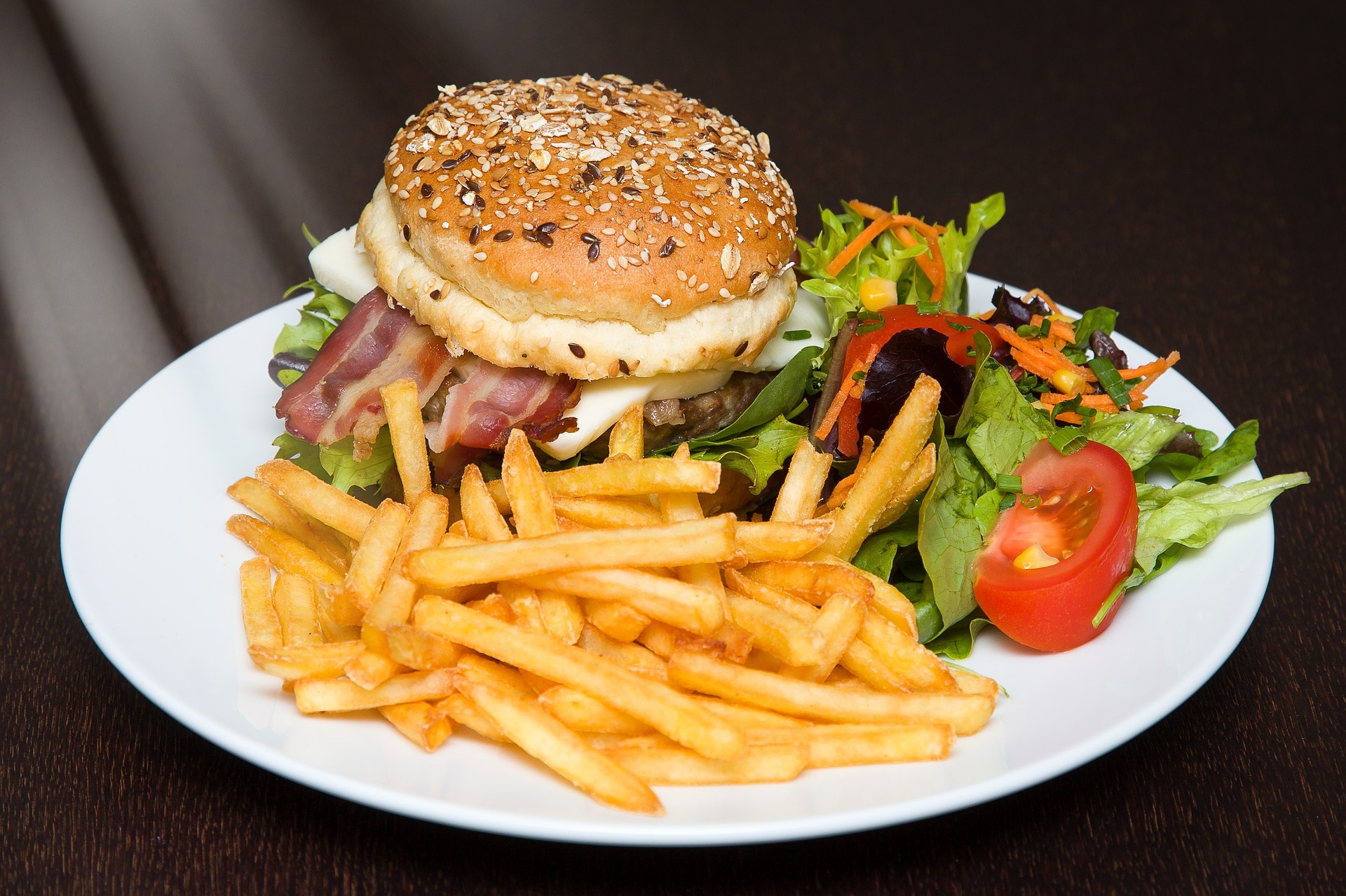 A burger with a variety of toppings on a plate with a small salad and french fries