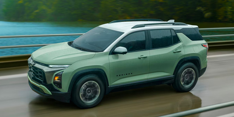 A green Chevrolet Equinox driving on a road near water.
